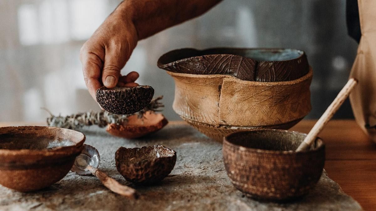 Manos del chef sobre cuencos de barro con ingredientes, a imagen de un yacimiento arqueol&oacute;gico
