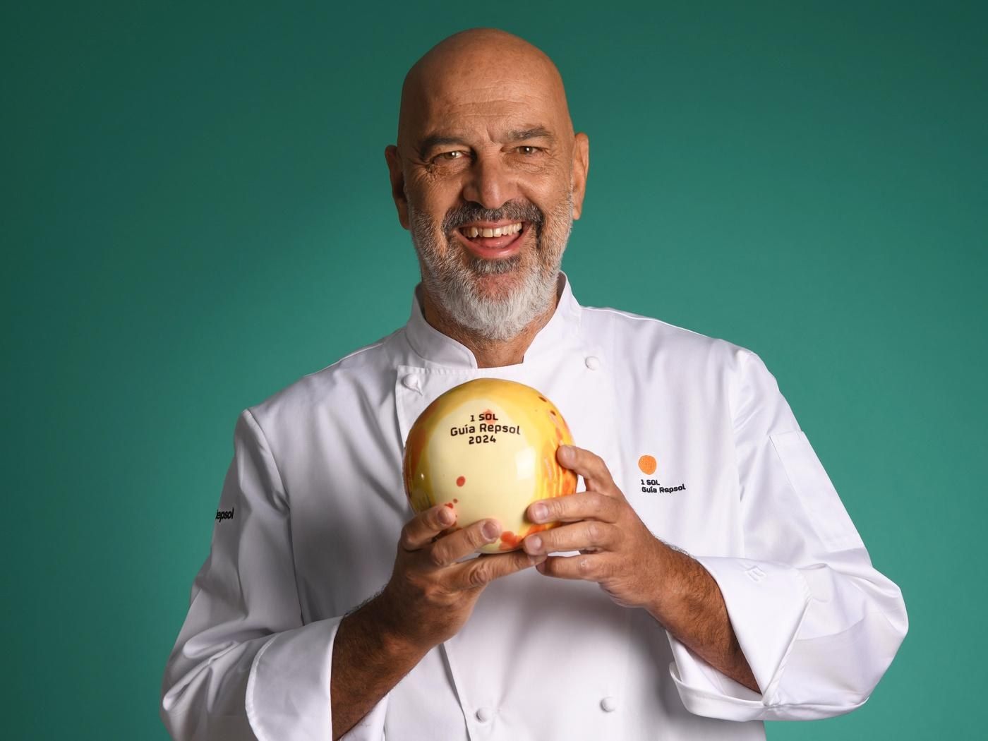 Retrato de Marcos Tavi&oacute; sonriendo y sosteniendo un plato esf&eacute;rico con el sello 1 Sol Gu&iacute;a Repsol 2024