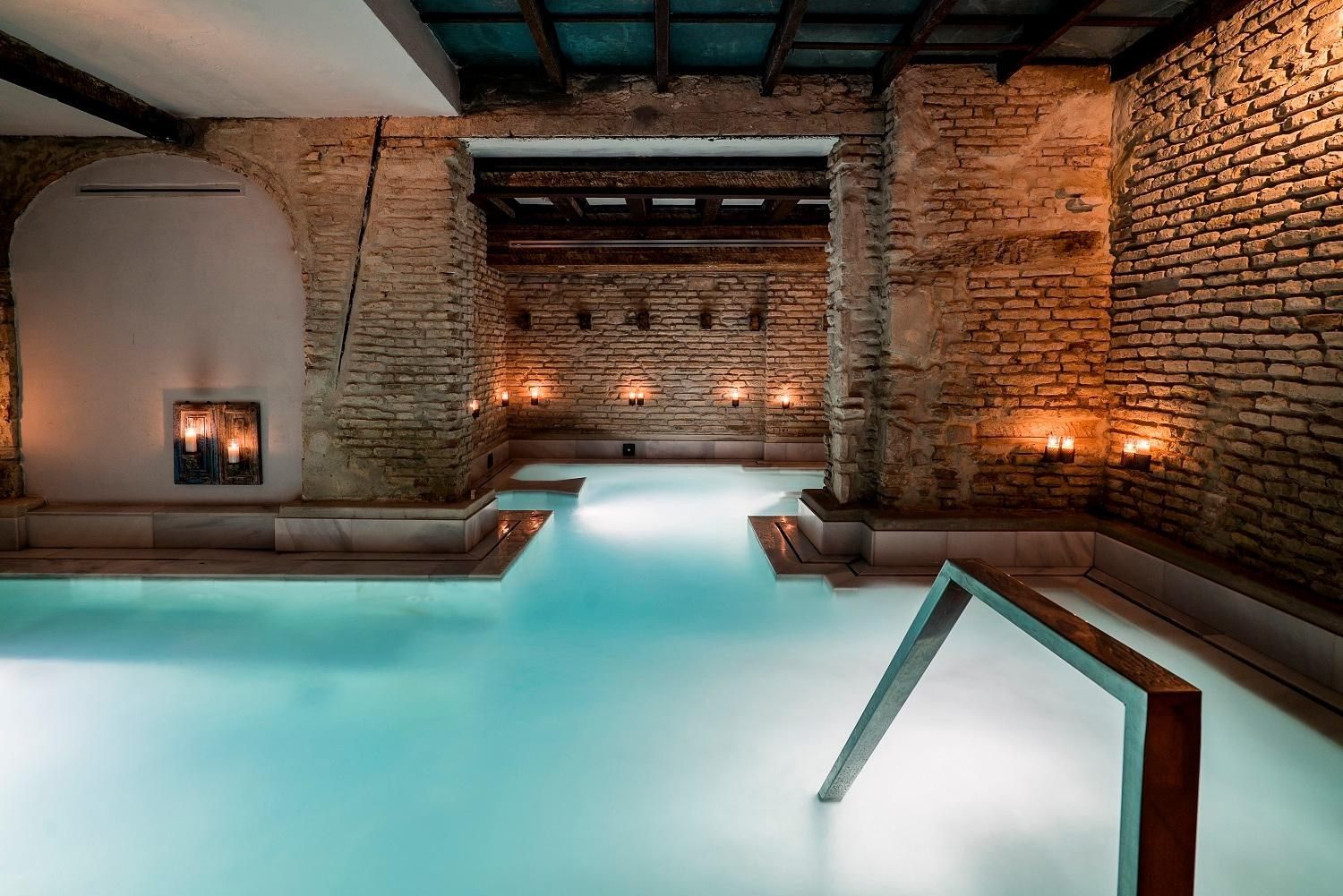 Interior de los ba&ntilde;os AIRE iluminado por velas bajo arcos romanos