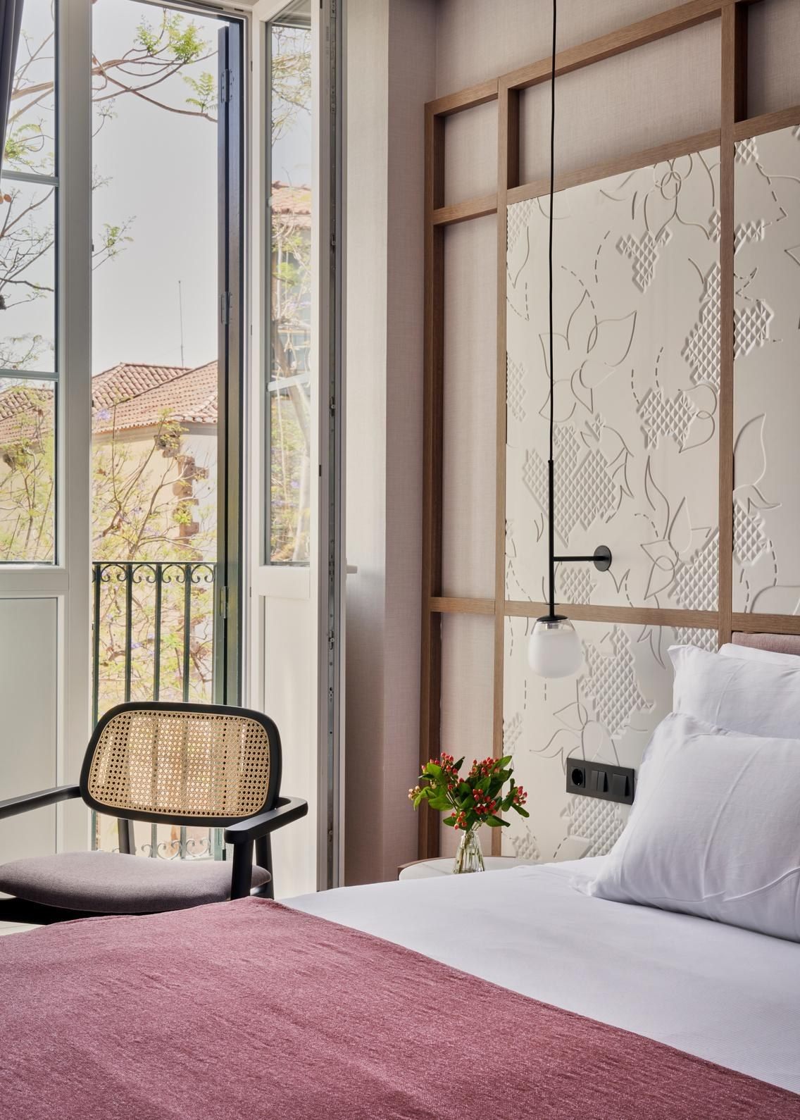 Habitaci&oacute;n con cama y silla de mimbre junto al balc&oacute;n