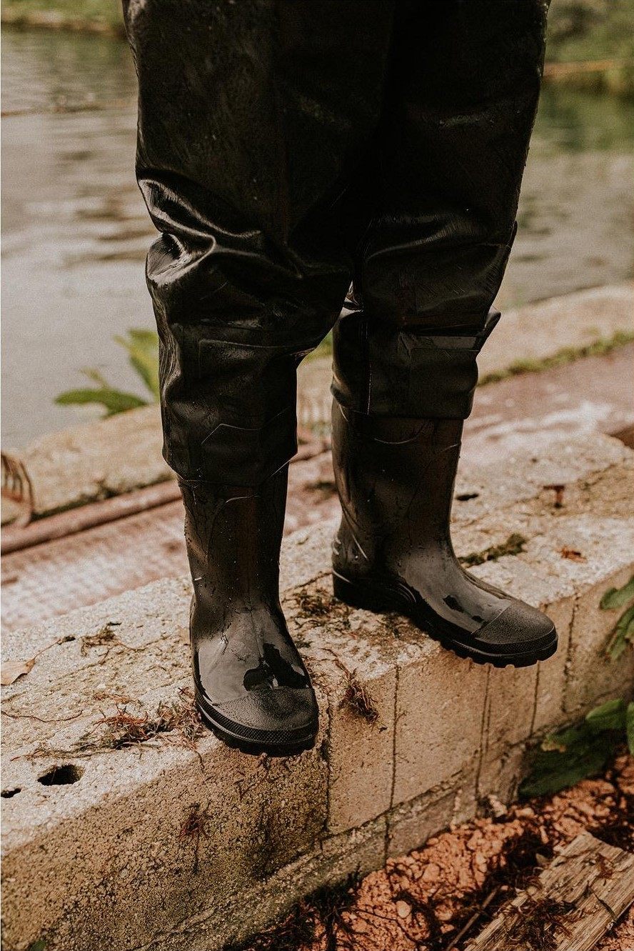 Botas de goma negras de pescador apoyadas sobre la piedra junto al agua